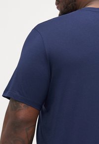 T-shirt blu navy a maniche corte realizzato in tessuto morbido, con scollatura rotonda e texture liscia; cuciture visibili sulle maniche e sull'orlo.