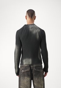 Mörkgrön ribbad tröja med långa ärmar, har en rund halsringning och textilstruktur. Utrustad med urtvättade grå jeans med bakfickor.