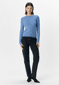 Ljusblå ribbad stickad tröja med lång ärm, ihop med svarta snäva jeans och spetsiga svarta ankelstövlar.