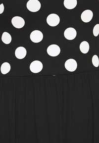 Musta mekko, jossa on valkoinen pilkkukuviointi yläosassa ja kerrostettu musta hame. Pehmeä, joustava kangas, jossa sileä pinta.