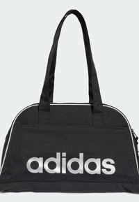 Musta kangaslaukku sisältää hopeanvärisen Adidas-logon, kaksi kahvaa sekä vetoketjukiinnityksen. Laukussa on valkoiset korostusviivat reunoilla.