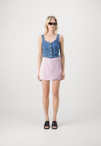Denim crop top med knapper, rosa satin miniskjørt og svarte slip-on sko. Glatt tekstur, tettsittende design og tydelig fargekontrast.