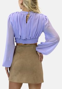 Blusa viola a metà con maniche lunghe plissettate, vita arricciata e schiena a chiave, abbinata a una gonna aderente in suede beige.