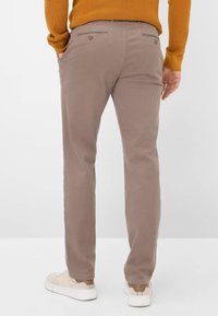 Pantalons en coton beige à coupe slim, avec poches arrière à boutons et texture lisse, associés à des baskets de couleur claire.