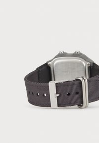 Bracelet de montre en tissu gris avec boucle en métal et quincaillerie argentée. Boîtier de montre rectangulaire avec surface texturée et bords arrondis.