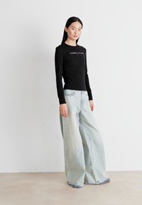 Crna majica dugih rukava s logotipom "Tommy Jeans", uparena sa svijetloplavim širokim trapericama s izblijedjelim opranim izgledom i istrošenim rubovima.