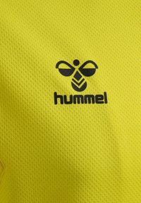 Gul tekstil med et struktureret, åndbart design. Har et sort "hummel" logo og et bi-emblem ovenfor.