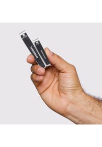 Mano che tiene due tagliaunghie neri Tweezerman, uno grande e uno piccolo, su uno sfondo grigio chiaro uniforme.