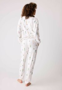Vitt pyjamaset med ett upprepat mönster av champagneflaskor och blommiga accent. Tyget verkar mjukt och lätt, med en avslappnad passform.