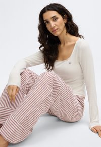 Bijeli dugi top s okruglim izrezom, uparen s ružičastim i bijelim prugastim, širokim hlačama za spavanje koje imaju mekanu teksturu.