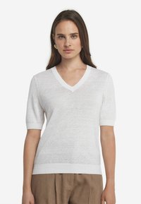 Hvid kortærmet v-hals sweater lavet af letvægts, struktureret stof. Ribbede kanter ved halsudskæringen og ærmerne, parret med løse beige bukser.