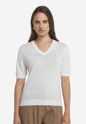 Hvid kortærmet v-hals sweater lavet af letvægts, struktureret stof. Ribbede kanter ved halsudskæringen og ærmerne, parret med løse beige bukser.