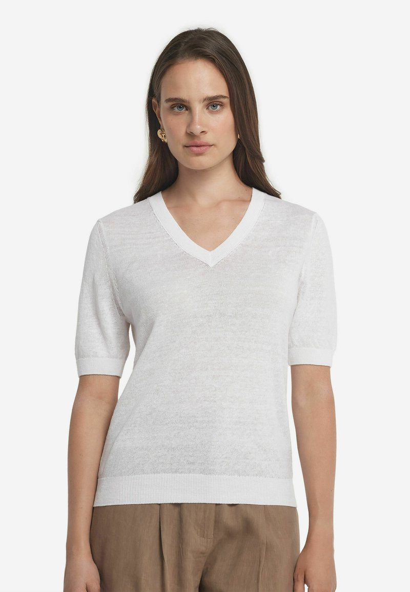 Hvid kortærmet v-hals sweater lavet af letvægts, struktureret stof. Ribbede kanter ved halsudskæringen og ærmerne, parret med løse beige bukser.