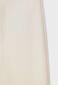 Tissu beige à côtes avec une texture lisse ; présente un motif de rayures verticales subtiles et une coupe droite. Aucun matériel proéminent visible.