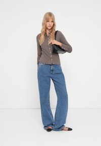 Långärmad brun skjorta med knappar, i kombination med lösa blå denimjeans. En svart axelremsväska och spetsiga svarta ballerinas fulländar outfiten.