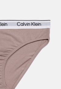 Μπεζ εσώρουχο Calvin Klein με λευκή ελαστική μέση που φέρει μαύρο λογότυπο της μάρκας, παρουσίαζόμενο σε λευκό φόντο.
