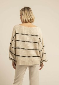 Pull en tricot surdimensionné couleur crème avec des rayures noires horizontales. Présente un col large, des épaules tombantes et des finitions côtelées. Texture douce.