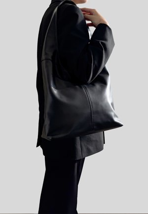 Czarna skórzana torba na ramię o gładkiej teksturze, dużym kształcie i pojedynczym pasku, z subtelnymi detalami ściegów wzdłuż boków.