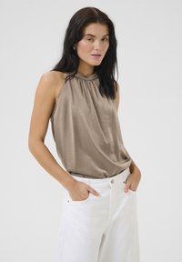 Světle hnědý hedvábný halter top s nařaseným výstřihem, doplněný bílými kalhotami s vysokým pasem a širokými nohavicemi. Hladká textura, minimalistický design.