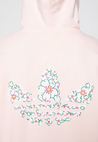 Retro di una felpa con cappuccio rosa pallido con motivo floreale che forma un logo trifoglio stilizzato nei colori verde, bianco, rosa e giallo.