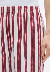 Pantalon en coton rayé rouge et blanc avec une taille élastique, présentant une texture lisse et des rayures verticales de largeurs variées.