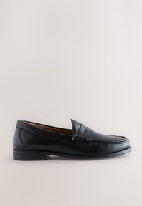 Mocassin en cuir noir à enfiler avec talon bas et détail d’une bride penny, présenté de profil sur un fond clair uni.