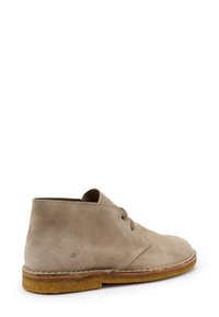 Botas de tobillo de ante beige con punta redondeada, dos ojales para cordones y suela de goma texturizada. Marca mínima cerca del talón.