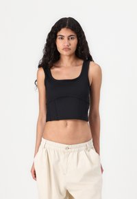 Črn rebrast crop top s kvadratnim izrezom, oprijet kroj in šivi na pasu, v kombinaciji z bež ohlapnimi hlačami.