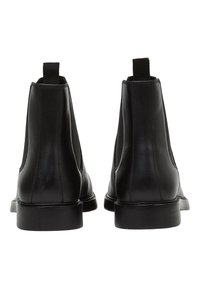 Stivali alla caviglia in pelle nera con pannelli elastici laterali, suole piatte e linguette sul retro. Texture liscia con dettagli di cucitura minimi.
