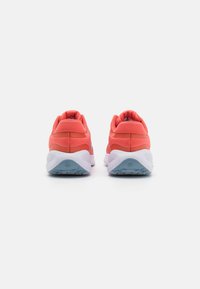 B baskets de sport corail avec un talon rembourré et une semelle extérieure blanche, présentant un design épuré et un tissu texturé sur le dessus.