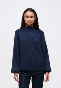 Granatowy sweter z ribbowanym splotem, o wysokim kołnierzu, szerokich r�ękawach i luźnym kroju, wykonany z teksturowanej, miękkiej przędzy.