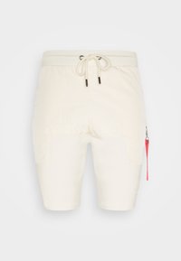 Shorts de couleur crème en tissu léger, dotés d'une taille élastique ajustable, de poches latérales et d'un détail de tirette rose.