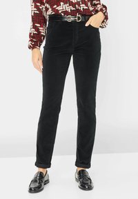 Zwarte corduroybroek met een slim fit, heeft een hoge taille en opgerolde manchetten. Gecombineerd met een gebloemde blouse en zwarte loafers.