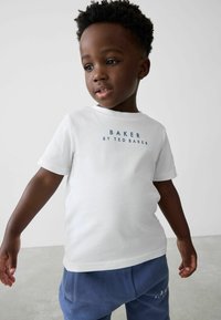 Valge puuvillane T-särk, millel on tumesinised tähed "BAKER BY TED BAKER", koostöös pehmete siniste dressipükstega. Lihtne disain ja lühikesed varrukad.