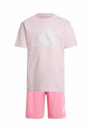 Due bambini sorridenti con magliette, pantaloncini e scarpe Adidas rosa abbinate, uno con un cappellino e l'altro con uno zaino nero.