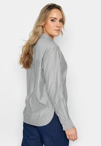Chemise à rayures grise clair et blanche. Dotée d'un empiècement au dos, de manches longues et d'un ourlet arrondi. Le matériau semble doux.