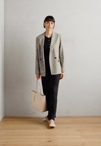 Gray textured blazer over a black shirt with buttons, black pants, and light beige tote bag, complemented by light shoes on wooden floor.