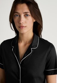 Zwarte pyjama's met witte bies, korte mouwen en een knoopsluiting kraag. Zachte, gladde textuur met een aansluitend ontwerp. Geen zichtbare patronen.