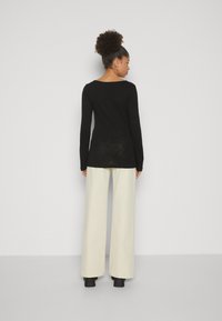 Haut noir à manches longues avec un col rond, associé à un pantalon crème à jambes larges et des bottes à talons noires. Texture lisse, détails minimes.