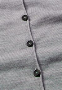 Close-up van grijs breiwerk met drie zwarte knopen in een verticale lijn genaaid.