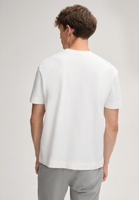 Biała koszulka z krótkim rękawem z gładkiej bawełny, cechująca się klasycznym okrągłym dekoltem i luźnym krojem, z prostym wykończeniem dołu. Pokazany widok z tyłu.