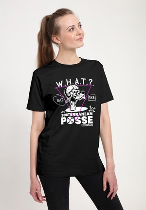 Kvinde med hestehale iført sort t-shirt med tegneserie-rat med hjelm og dryppende tunge, tekst "W.H.A.T.? Subterranean Posse SK8 Rat.