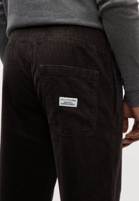 Pantaloni in corduroy marrone scuro con texture a righe verticali, tasca posteriore e un'etichetta con il marchio "Marc O'Polo Denim".
