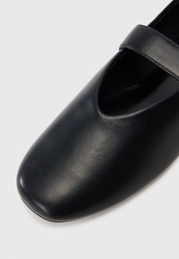Sapatos de couro pretos com bico redondo e design recortado. Apresentam uma tira única na parte superior para um ajuste seguro. Textura suave.