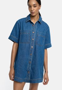 Sukienka koszulowa z dżinsu w jasnoniebieskim kolorze, z krótkimi rękawami, dwiema kieszeniami na piersiach i guzikami z przodu. Kontrastowe przeszycia wzdłuż szwów.