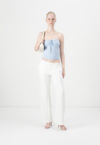 Top sem alças de cor azul clara com um laço na frente, combinado com calças brancas de perna larga e sandálias de salto em tom creme. Pequena mala pendurada no ombro.