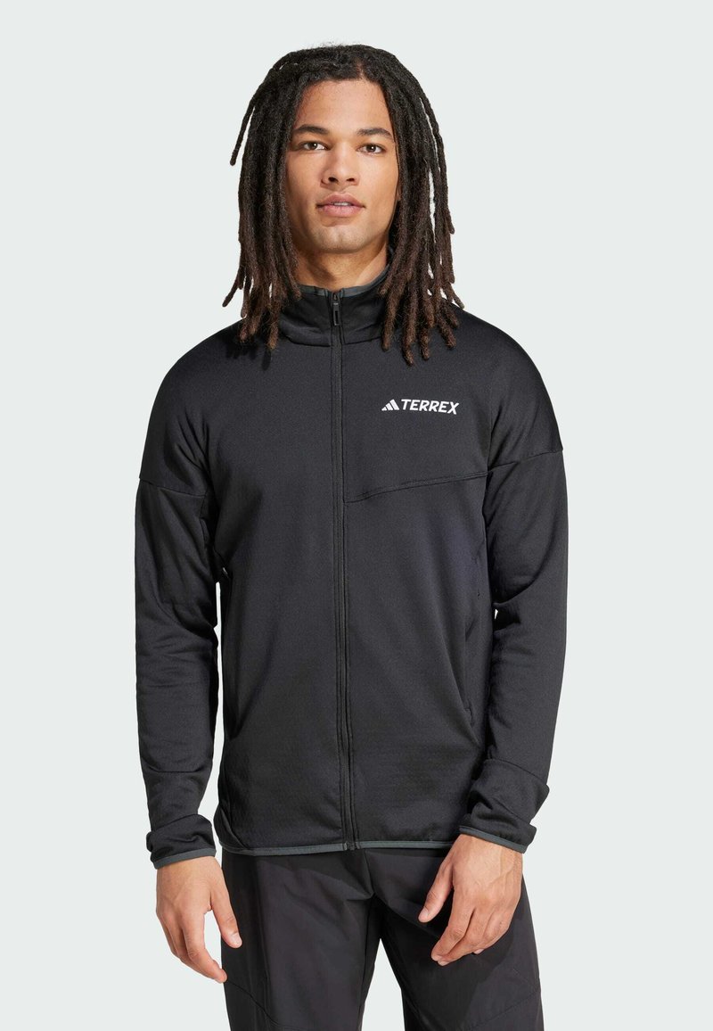 Jacket preta Terrex com fecho, gola alta, mangas longas e bolso no peito. Apresenta uma textura suave e um logótipo branco do lado esquerdo.