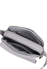 Lys grå crossbody-veske laget av mykt lær, med flere glidelåslommer, glatt tekstur og aksenter i sølvfarget metall.