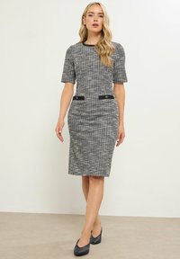 Schwarz-weiß gemustertes, tailliertes Kleid mit kurzen Ärmeln, runder Halslinie und schwarzen Akzenten an der Taille. Glatter, strukturiertes Material.