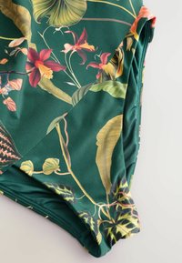 Costum de baie verde dintr-o singură piesă, cu un model floral ce include flori roșii și galbene și frunze verzi, fabricat dintr-un material sintetic neted.
